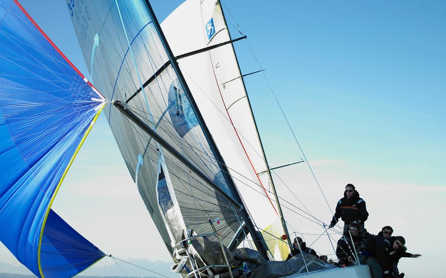Velero de regata navegando escorado en mar abierto, tripulación en la borda
