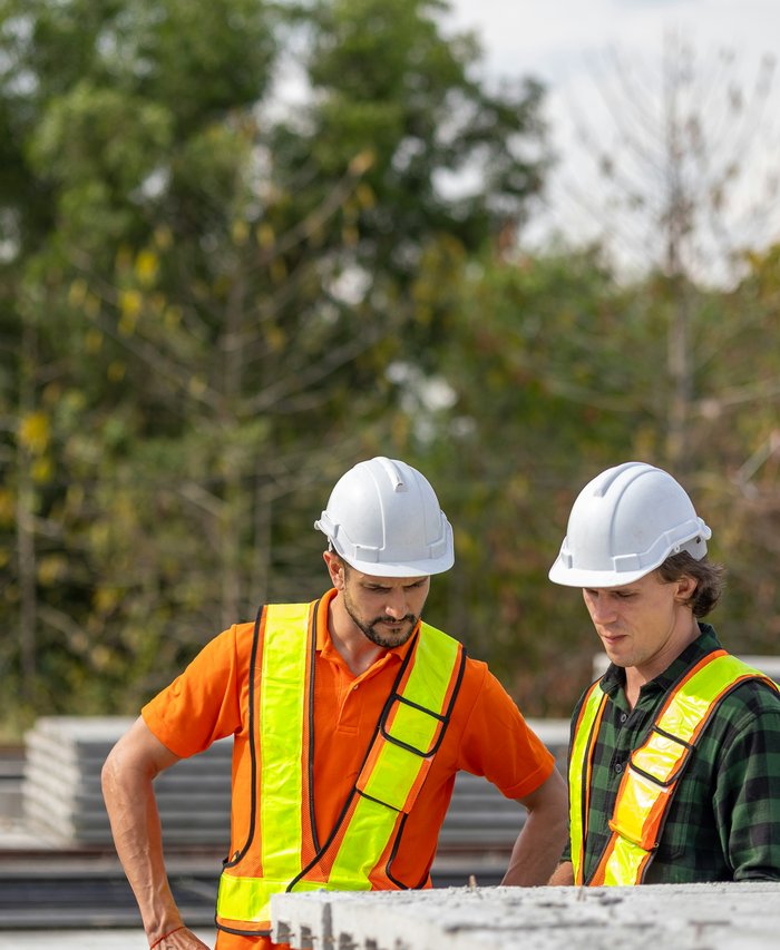 Dos constructores con casco revisando planos en una obra en construcción