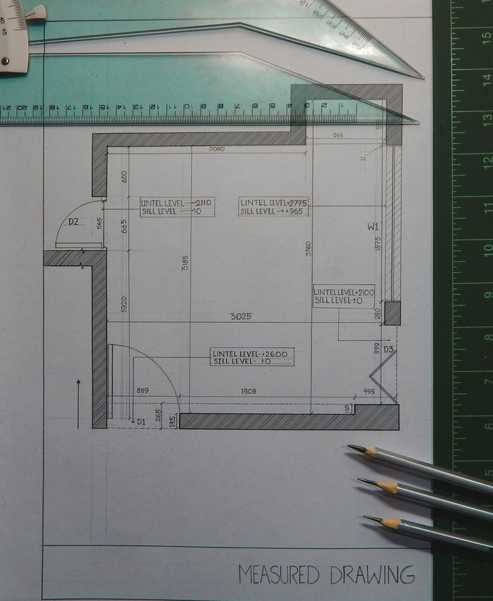 Plano medido de una vivienda sobre mesa de trabajo, con regla y escuadra